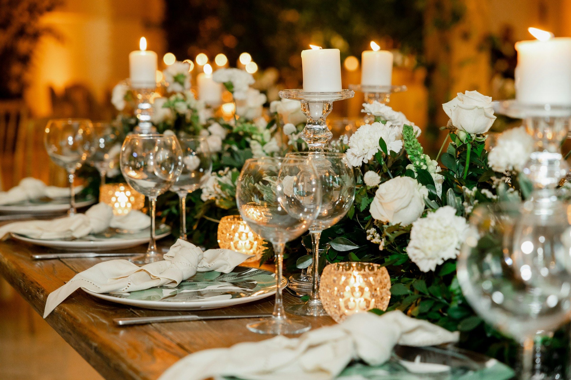 A candlelit table dressed with white roses, greenery and crystal glassware